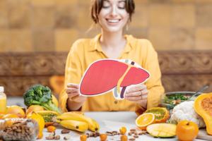 Woman holding a liver illustration surrounded by healthy foods good for liver health